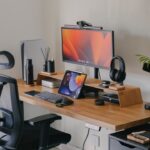 minimalist home office setup with a wooden desk, laptop, lamp, notebook, and soft natural light